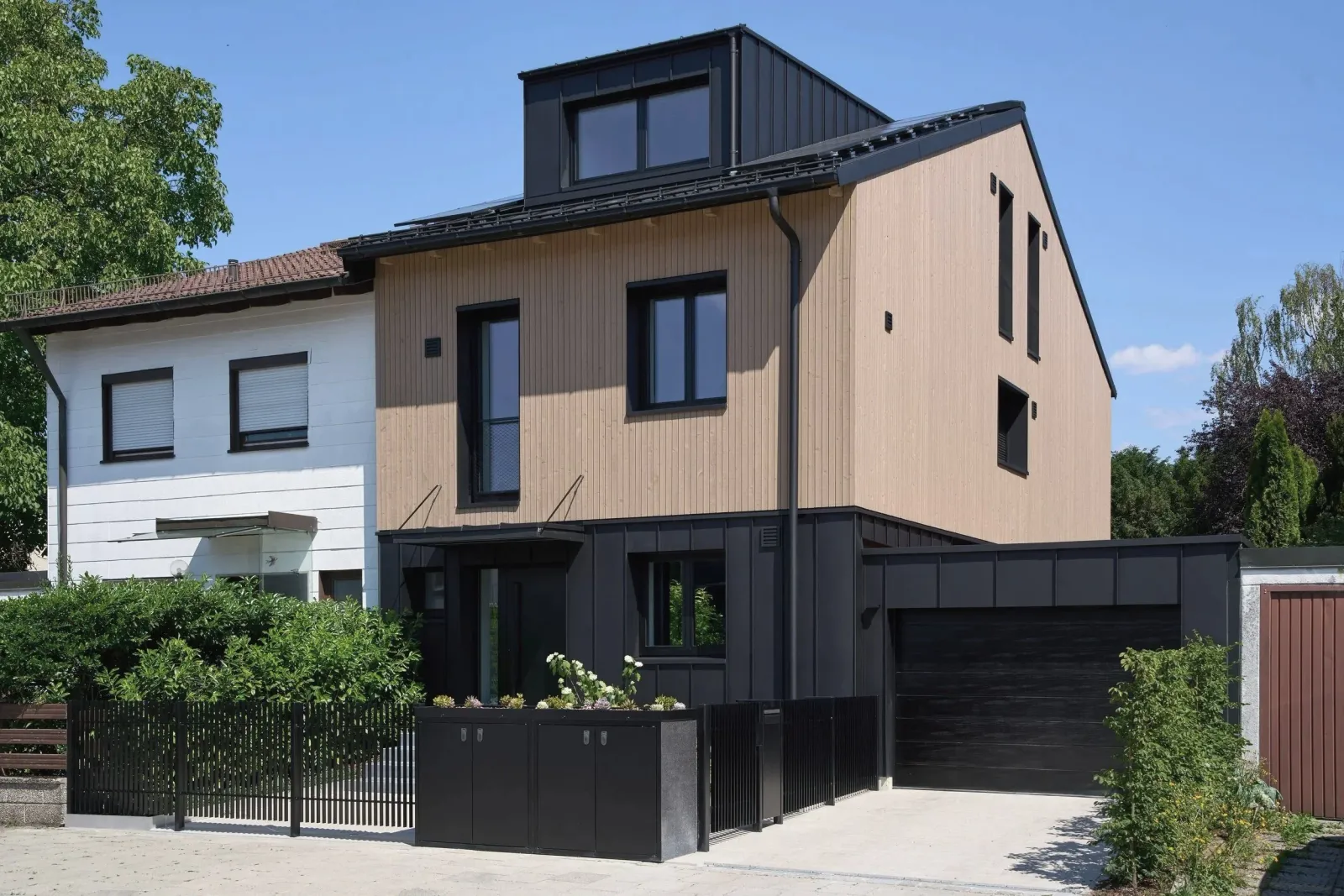 Straßenansicht mit Holzfassade, schwarzer Blechverkleidung und Garage