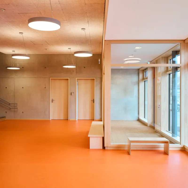 Foyer mit orangem Boden, Sitzstufen und Blick in den verglasten Gruppenraum