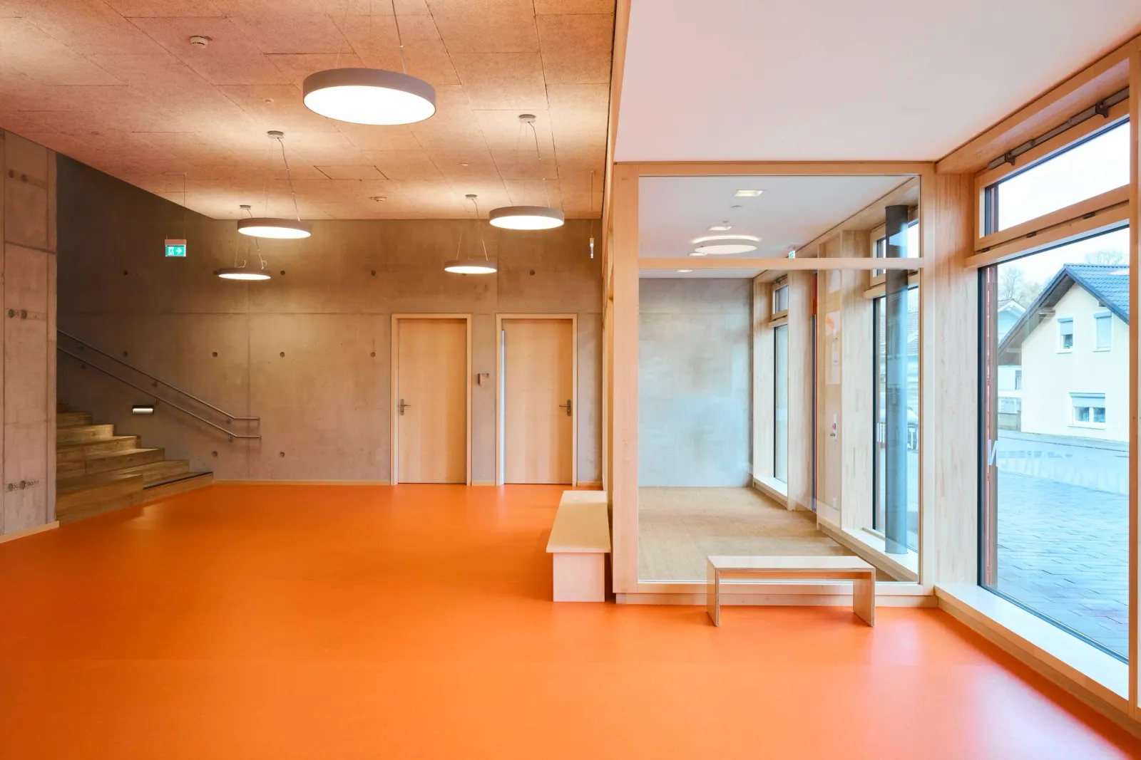 Foyer mit orangem Boden, Sitzstufen und Blick in den verglasten Gruppenraum
