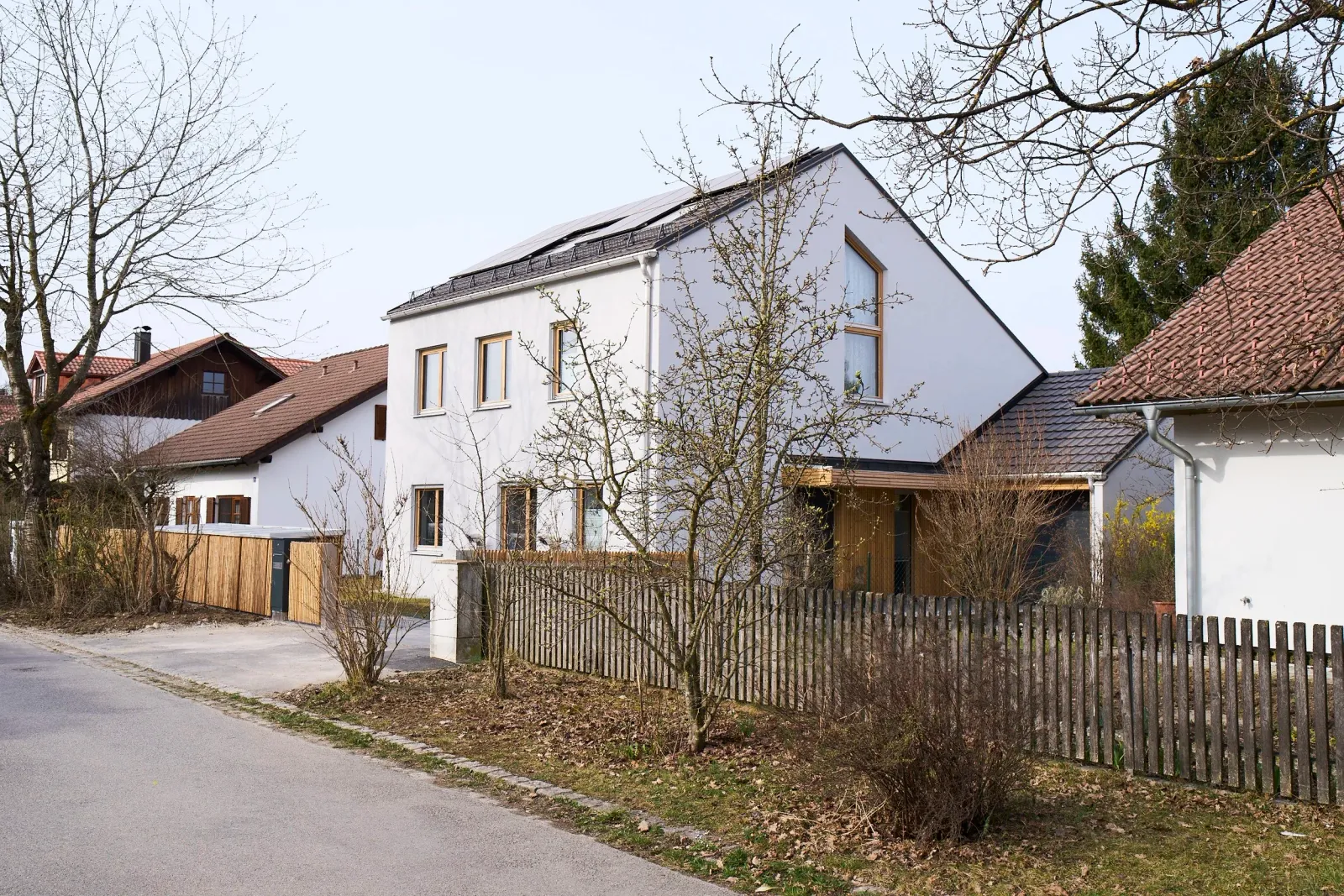 Straßenansicht mit Satteldach, Photovoltaikanlage und Holzlattenzaun