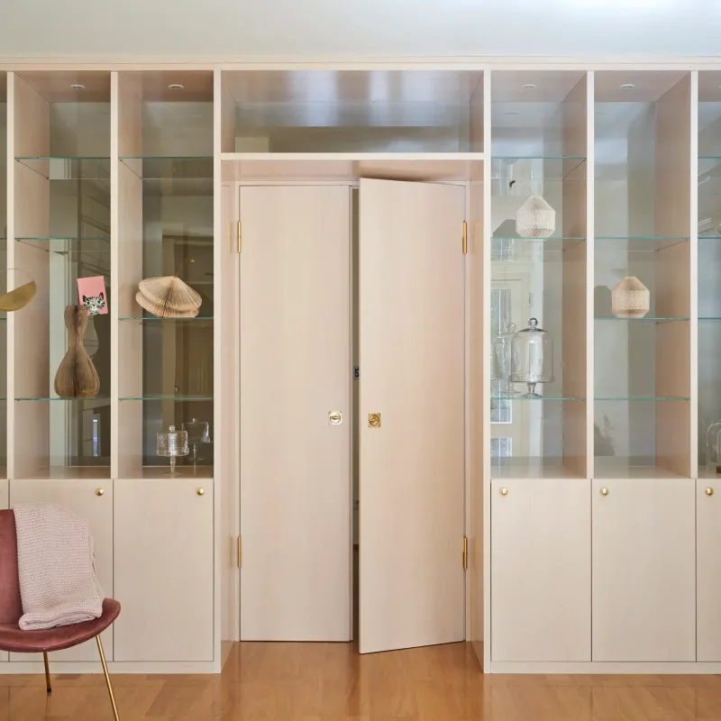 Wandregal mit Vitrinen, goldenen Accessoires und rosa Sessel