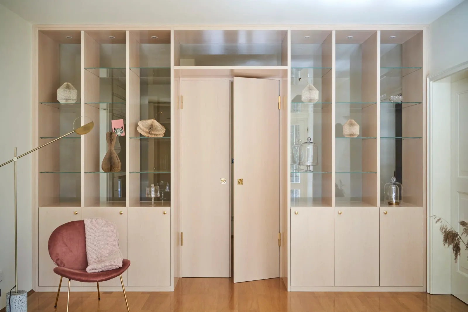 Wandregal mit Vitrinen, goldenen Accessoires und rosa Sessel