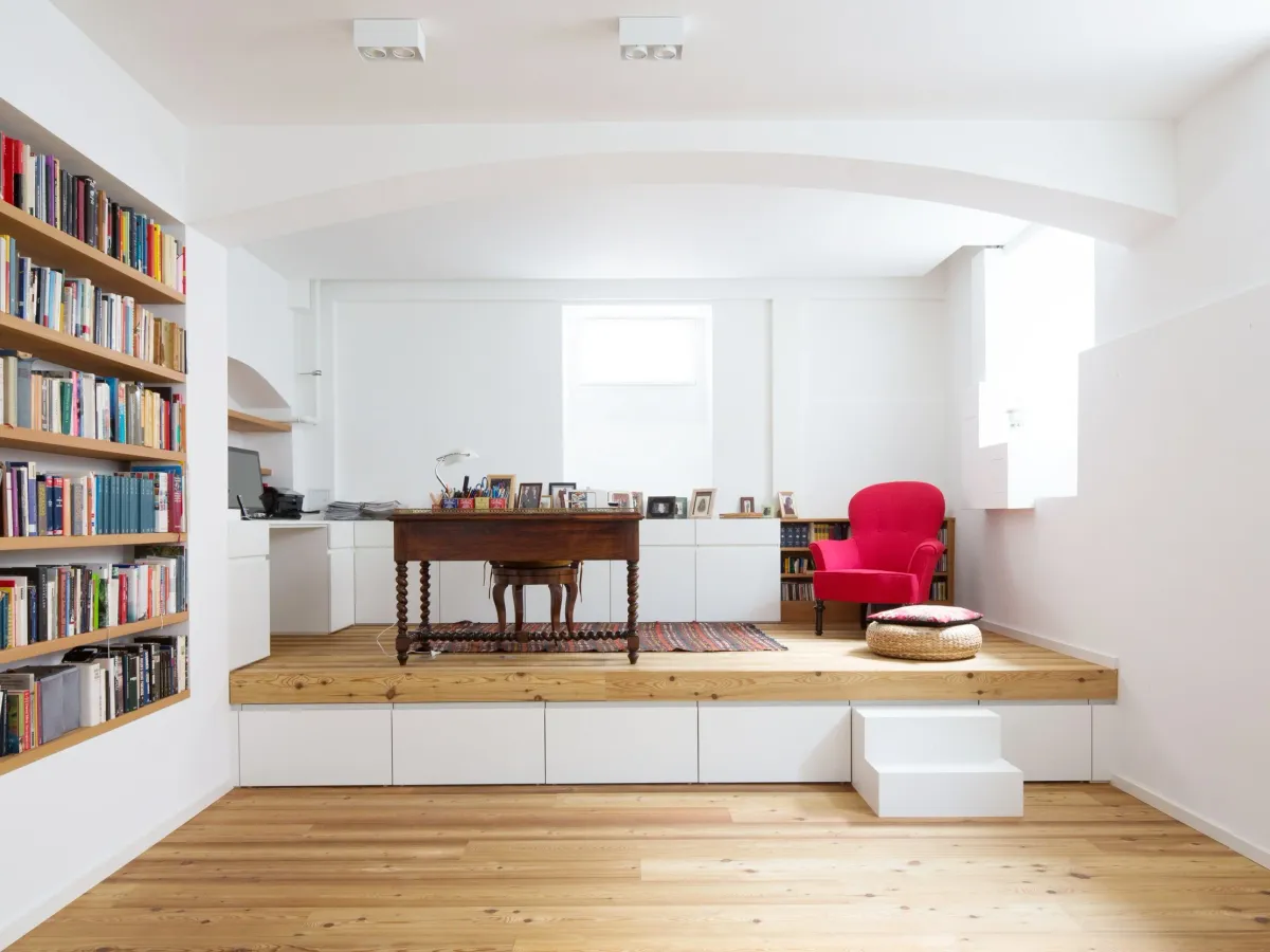Erhöhte Arbeitsnische mit Bücherwand, Antikschreibtisch und rotem Sessel