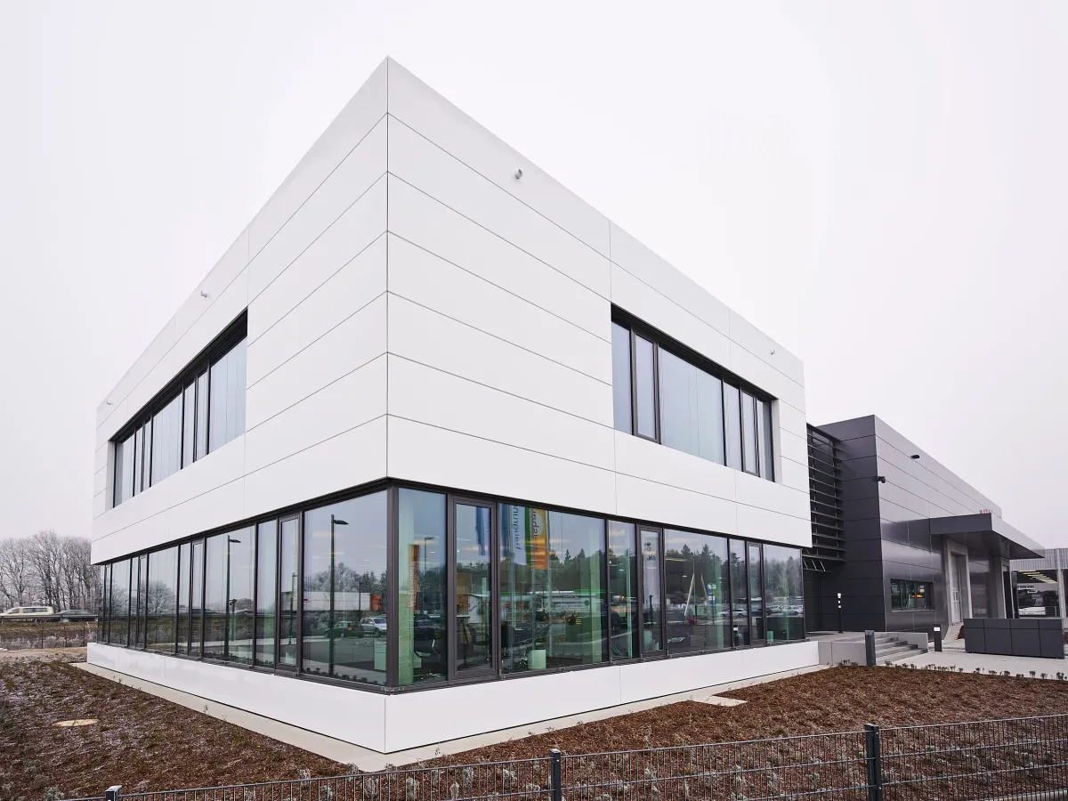 Eckansicht mit verglastem Erdgeschoss und Lagerhalle im Hintergrund
