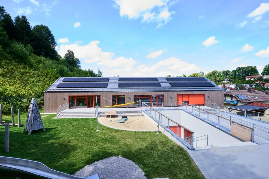 Blick über Spielwiese und Sandkasten zum Gebäude mit Photovoltaikdach