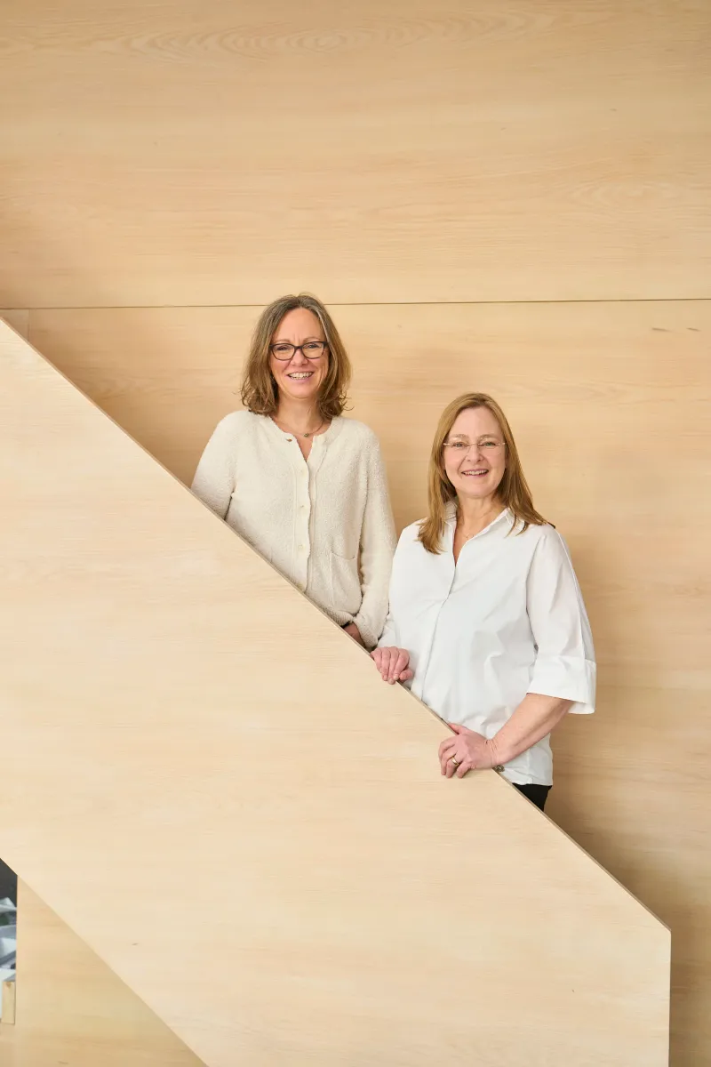 Eva Petri und Birte Raff, Gründerinnen von pur architekten, auf einer Holztreppe